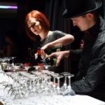 Two bartenders pouring wine into glasses at a bar