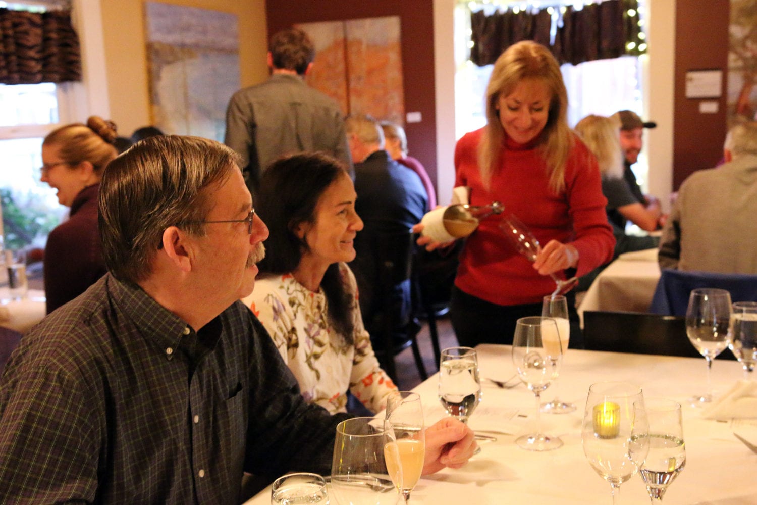 woman in a red sweater pouring wine for a table of restaurant guests