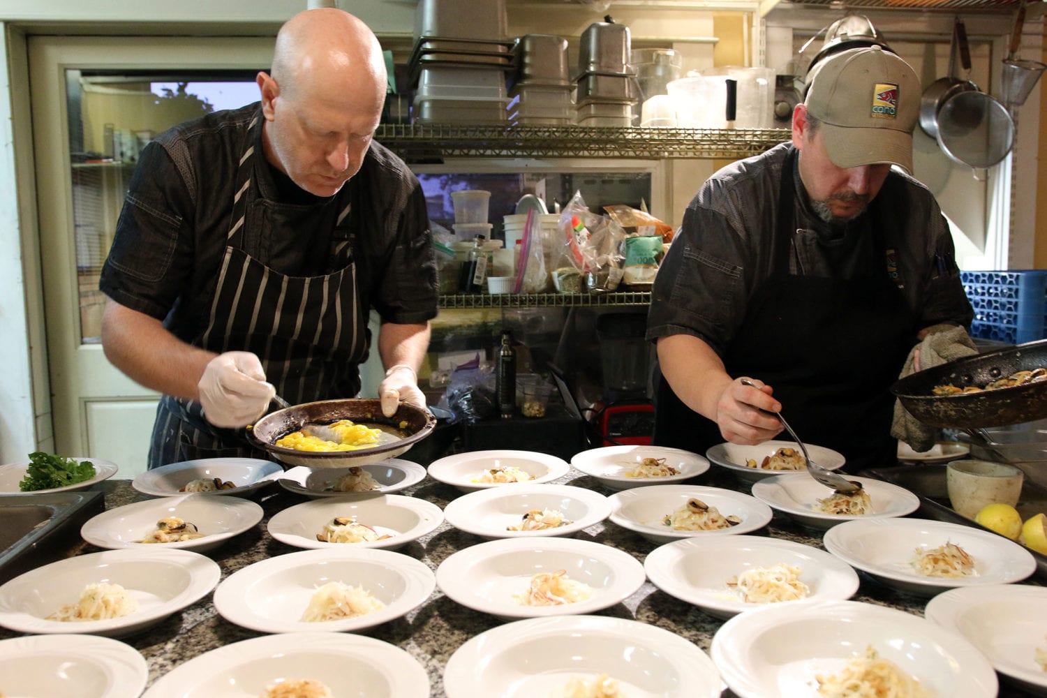 Two chefs plating entrees in a kitchen