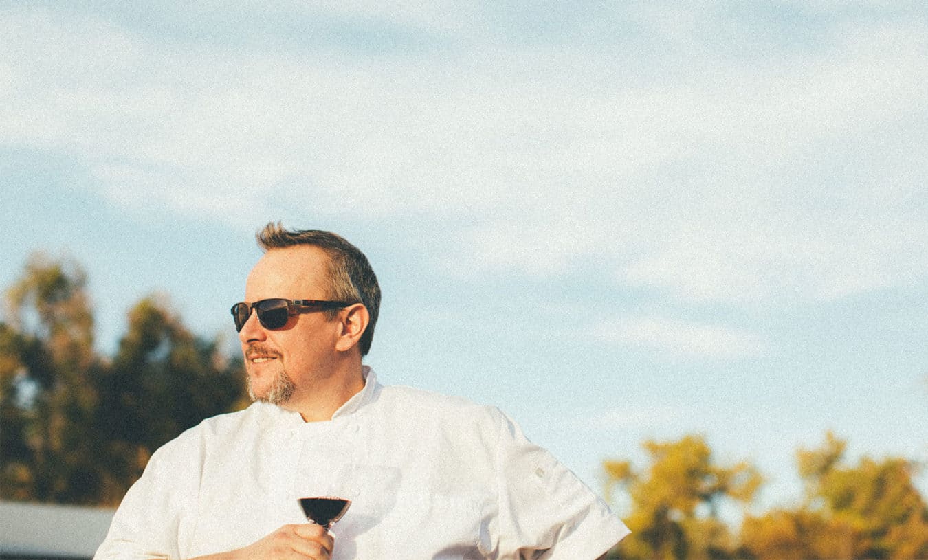 man in white chef coat wearing sunglasses and holding a glass of red wine