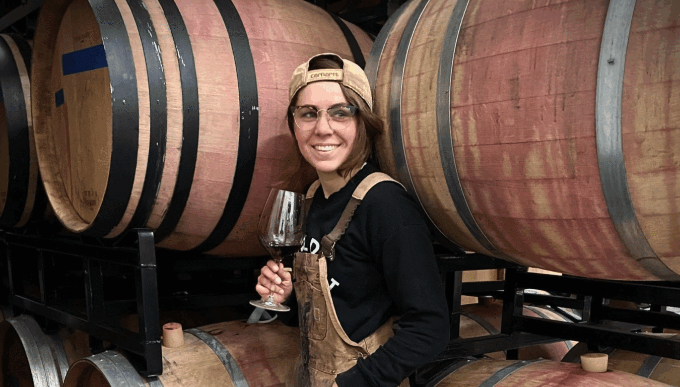 woman holding a glass of wine in front of wine barrels
